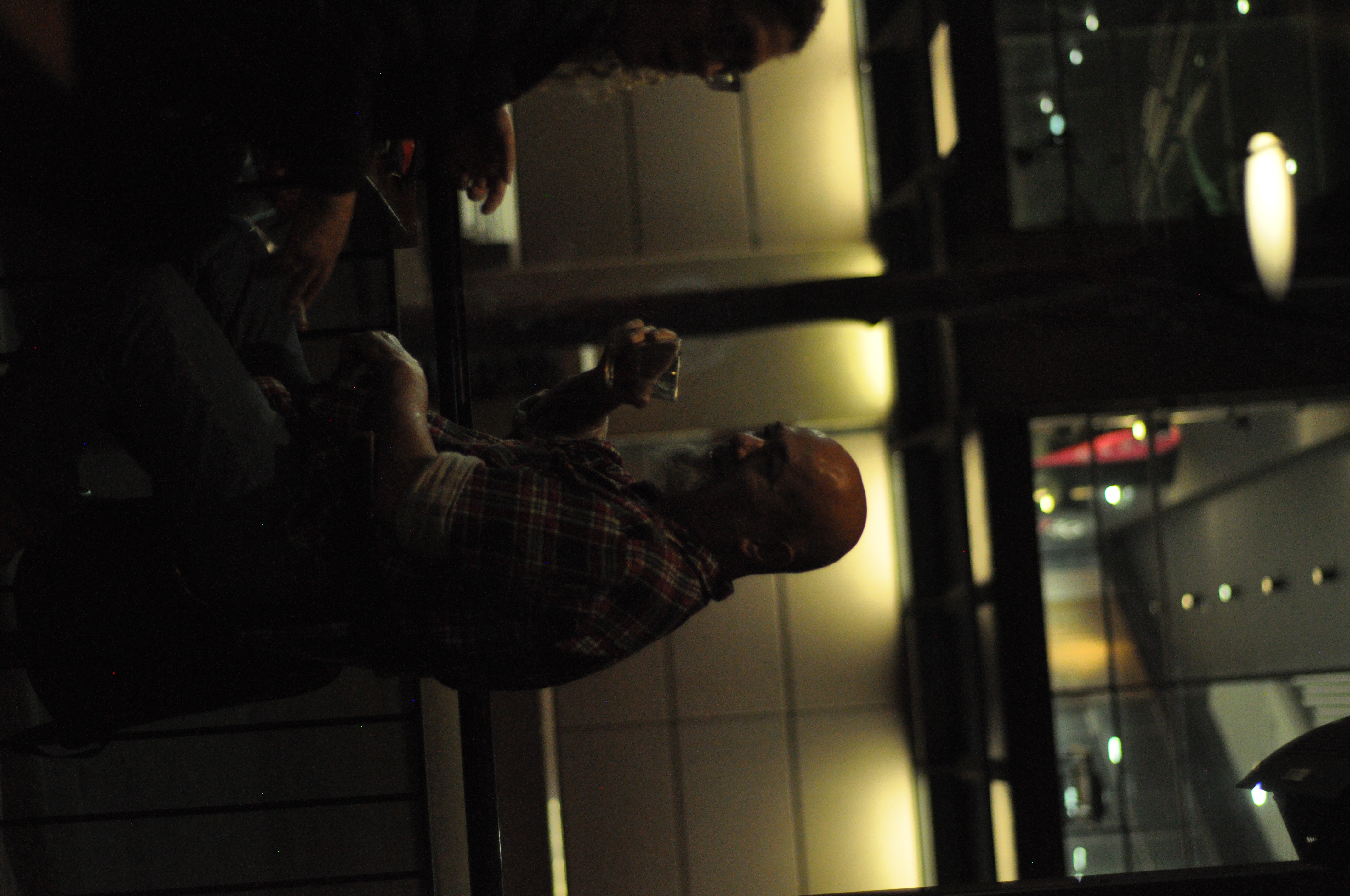 A man holding a drink beside a reflective window in a dimly lit venue