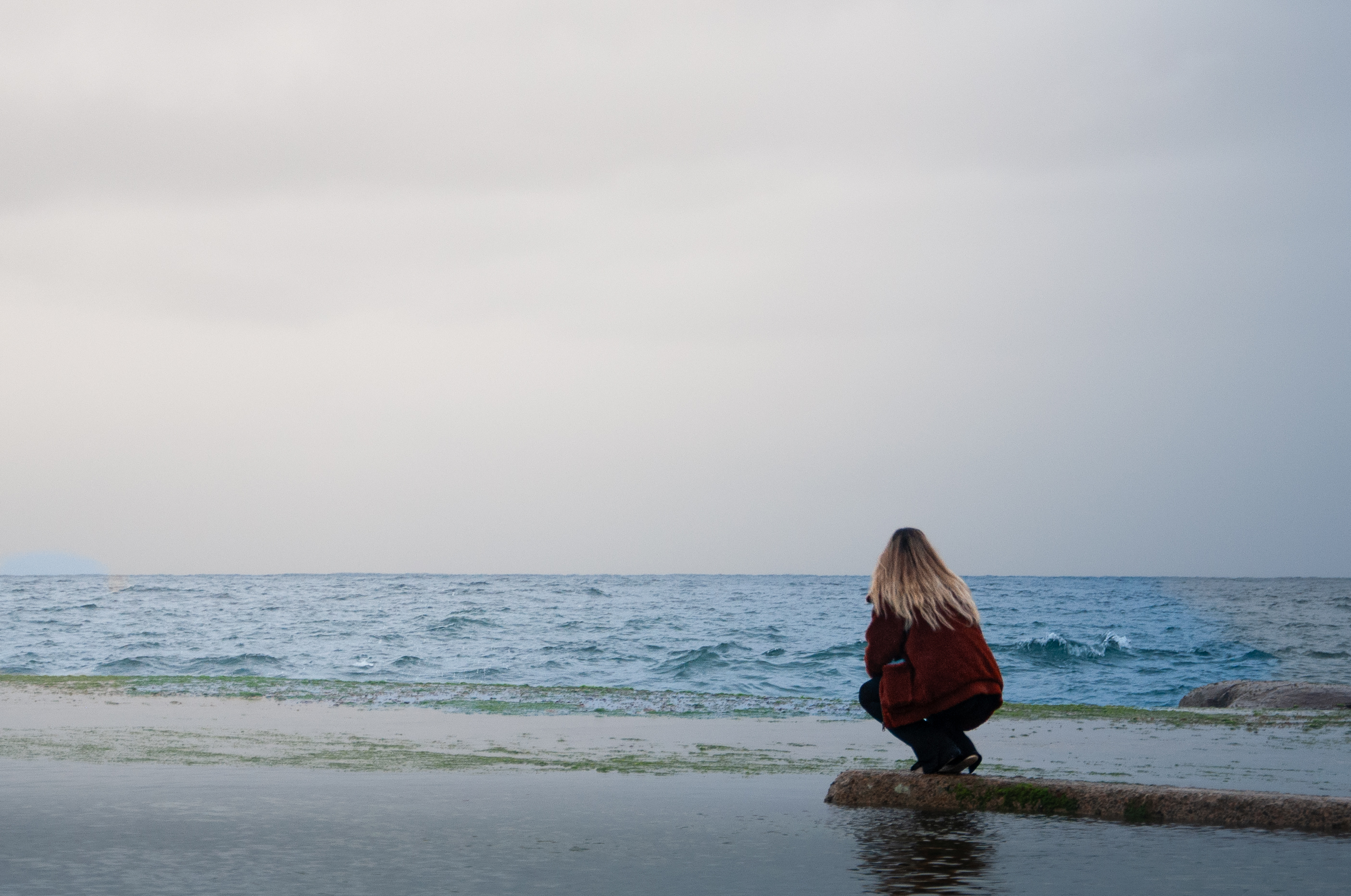 Person crouching beside the ocean